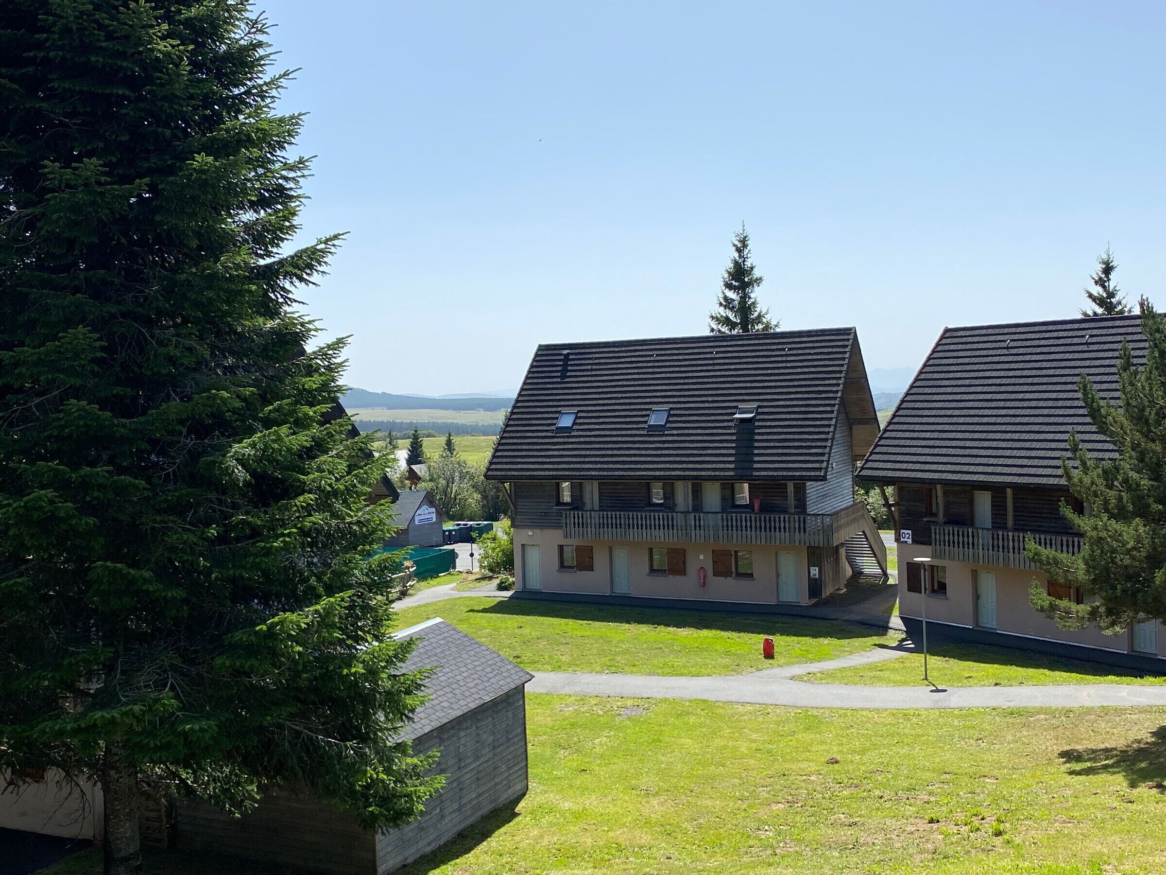 A row of traditional chalet-style buildings with sloped roofs, a central pathway, and a view of distant hills.