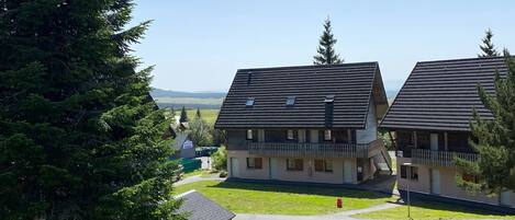 A row of traditional chalet-style buildings with sloped roofs, a central pathway, and a view of distant hills.