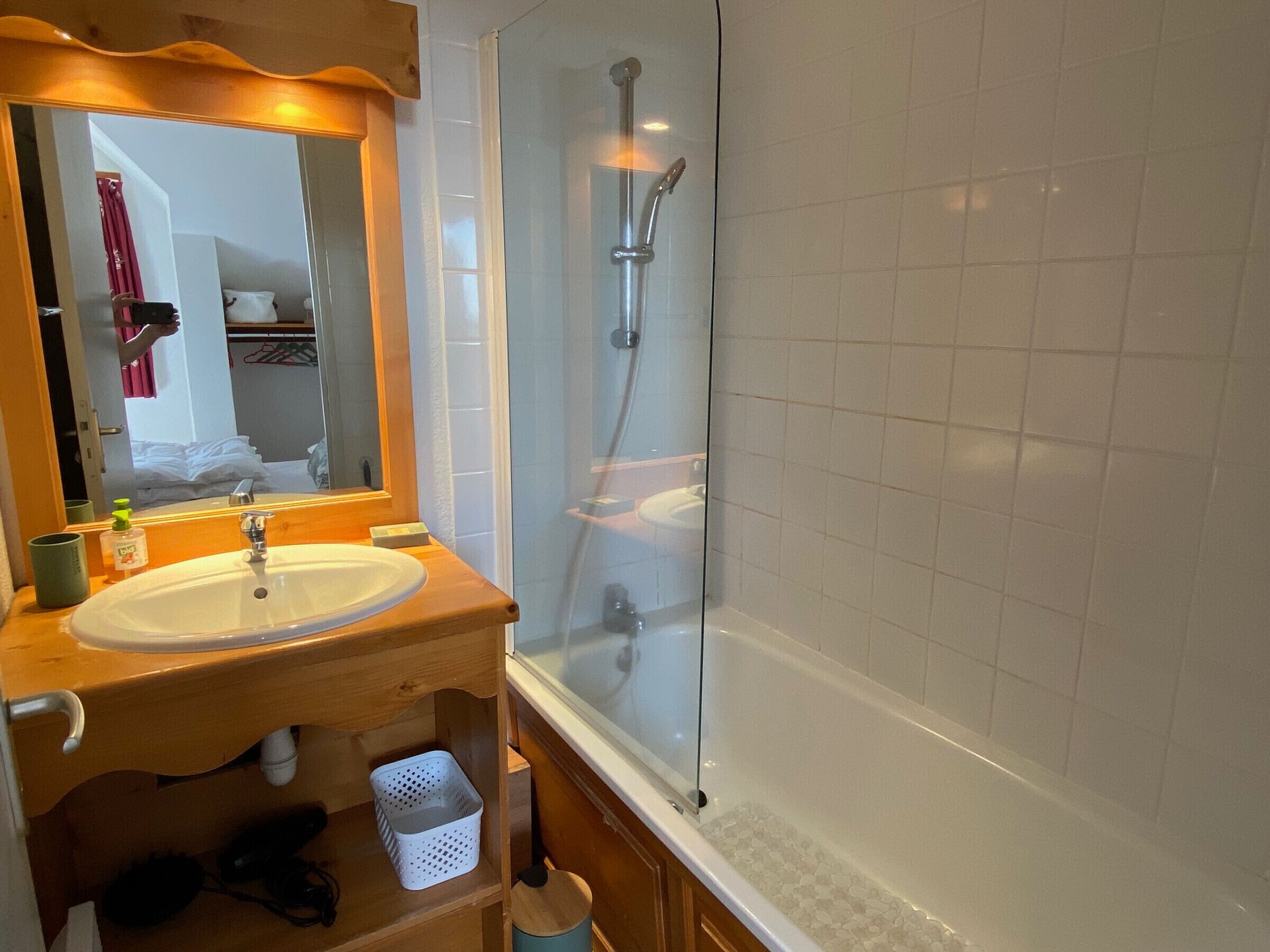 A bathroom with a wooden vanity, a glass shower enclosure, and a white tiled wall.