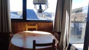 Een eetgedeelte met een ronde tafel, stoelen, een hanglamp en uitzicht op een stad door grote ramen.