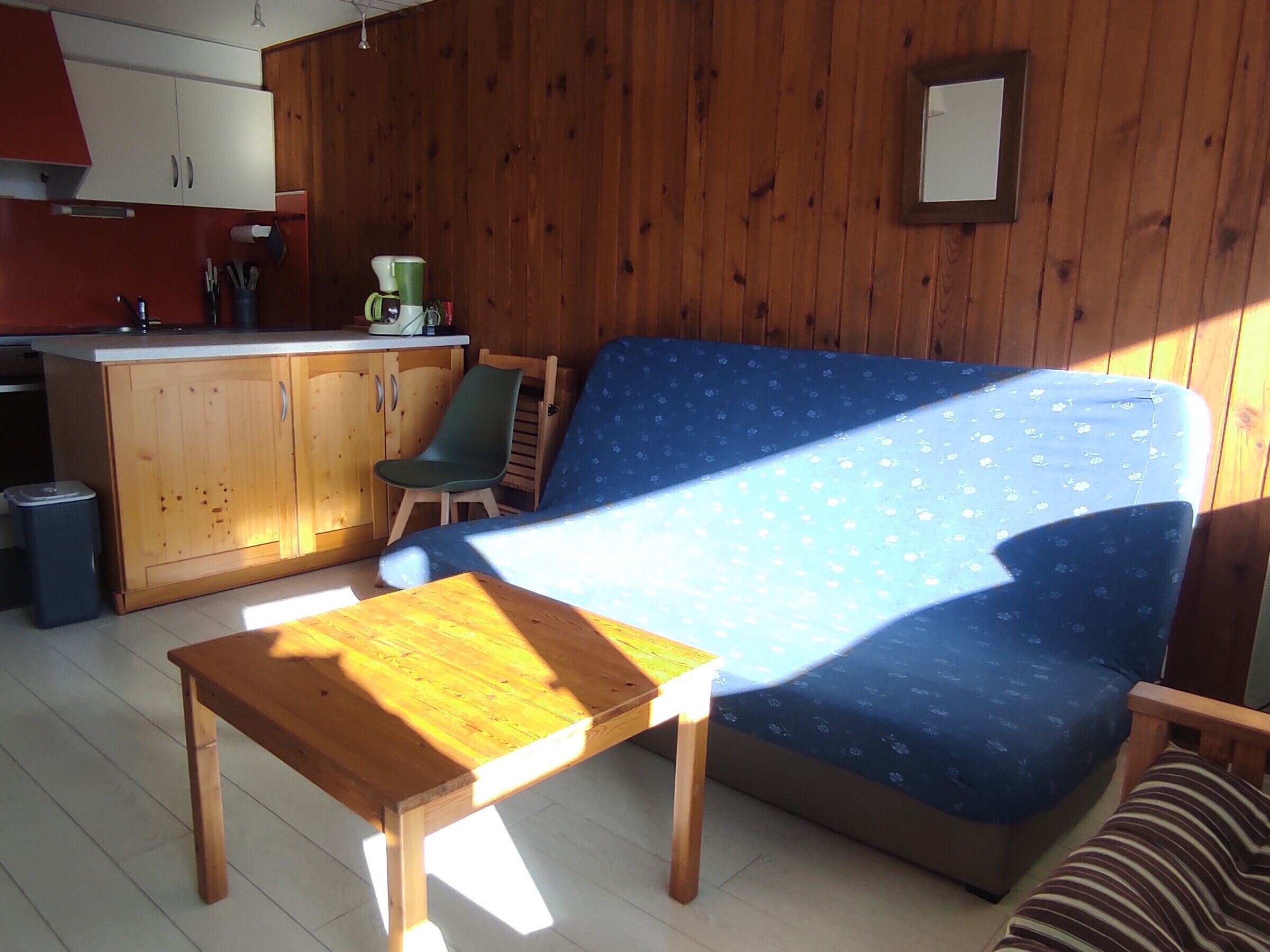 A living room with a sofa, a small table, a chair, wooden cabinets, and a kitchen area.