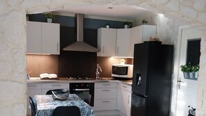 A kitchen with a stone wall, white cabinets, a black refrigerator, a microwave, and a dining table with chairs. - Cosy house just outside Tours  (Saint-Branchs)