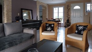 A living room with a grey sofa, two wicker armchairs with black and white cushions, a glass coffee table, and a dining area with a table and chairs. - Cosy house just outside Tours  (Saint-Branchs)