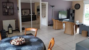 A spacious living room with a dining area, a kitchen in the background, and a large window. - Cosy house just outside Tours  (Saint-Branchs)