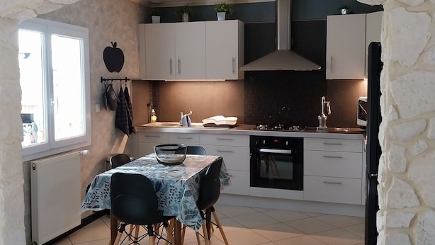 A modern kitchen with white cabinets, a stone archway, a dining table with chairs, and a view through a window. - Cosy house just outside Tours  (Saint-Branchs)