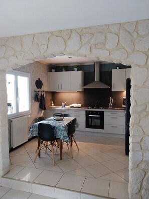 A modern kitchen with white cabinets, a stone archway, a dining table with chairs, and a view through a window. - Cosy house just outside Tours  (Saint-Branchs)