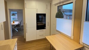 Eine moderne Küche mit weißen Schränken, einem eingebauten Backofen und einem Essbereich mit Holztisch und -stühlen.