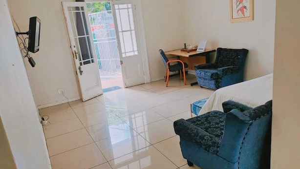 A room with a tiled floor, two blue sofas, a small table, and a door with a window. - Steps Guest House (Gqeberha (Port Elizabeth))