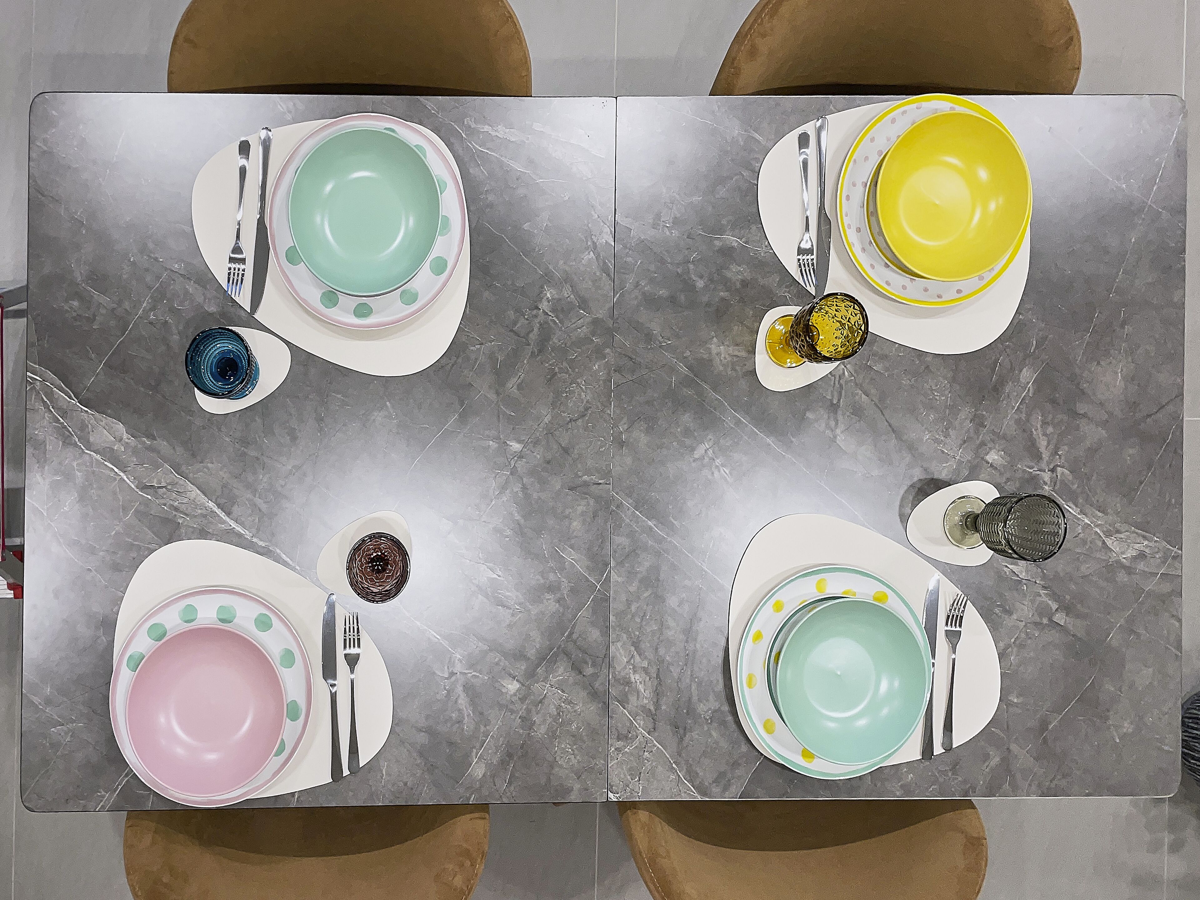 A dining table set with four plates, each with a different color and pattern, accompanied by cutlery and glasses.