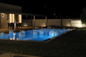 Una piscina con decoraciones esféricas, un área de estar cubierta y un edificio con el letrero "Elysium".