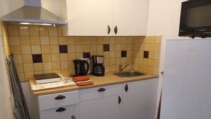 A compact kitchen with a microwave, kettle, and coffee maker on the counter, a sink, and a refrigerator.