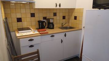 Een kleine keuken met een magnetron, waterkoker en koffiezetapparaat op het aanrecht, een spoelbak en een koelkast.