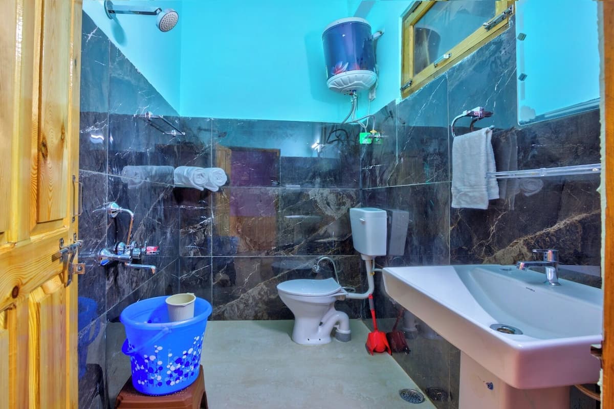 A bathroom with a toilet, sink, shower, and a blue bucket.