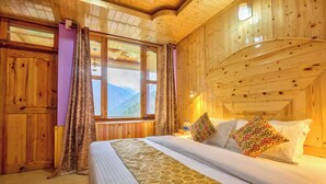 A wooden cabin room with a bed, curtains, and a window with a mountain view. - Tirthan Height - Facing toward Snow View (Banjar)