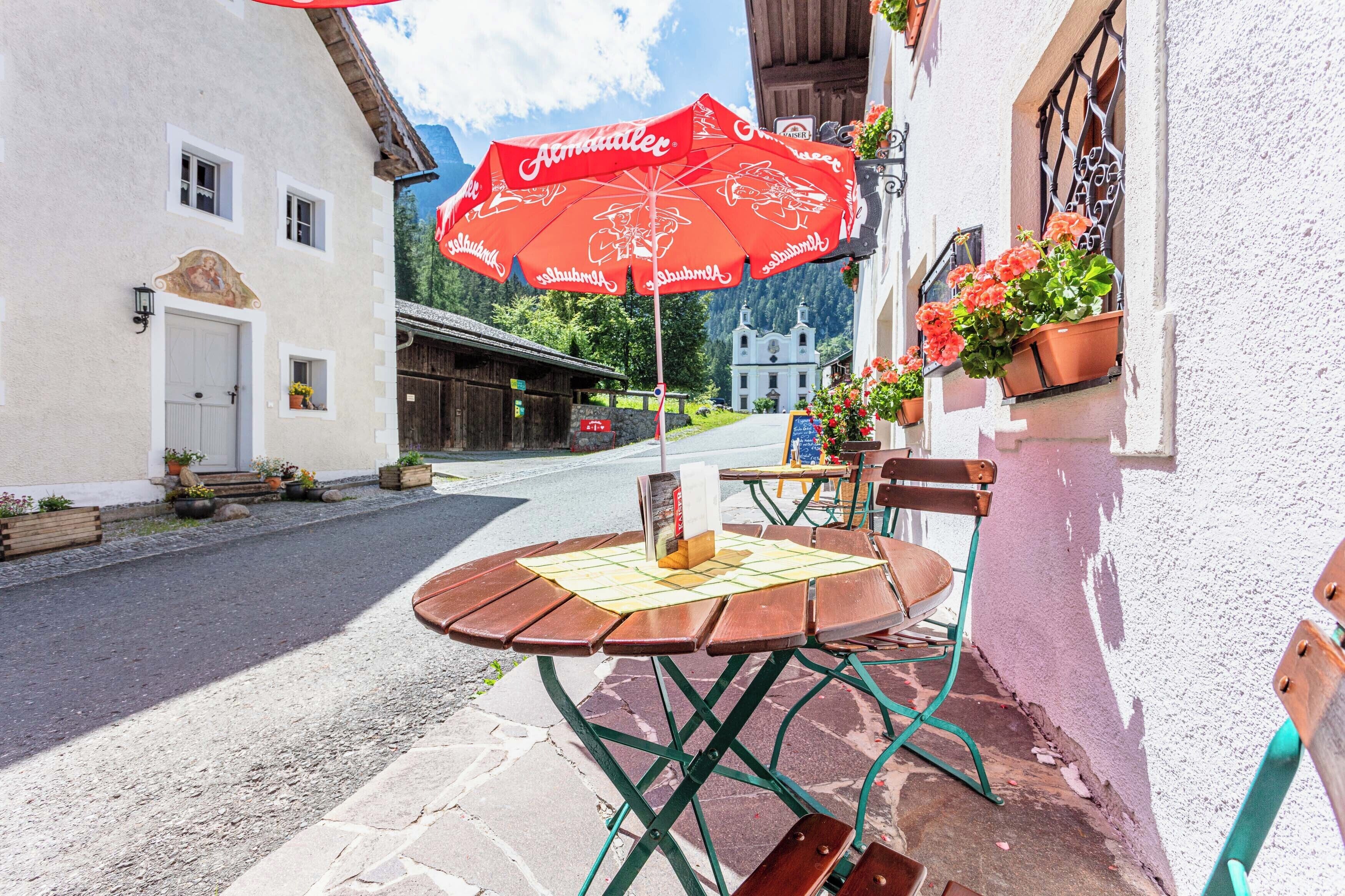 An outdoor seating area with a table and chairs, a red umbrella, and potted plants.