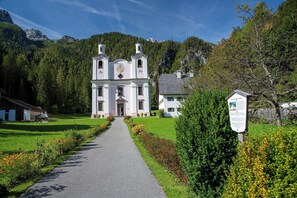 A church with a central entrance and two towers, surrounded by a well-maintained garden and a mountain backdrop. - Gasthof Maria Kirchental (Sankt Martin bei Lofer)