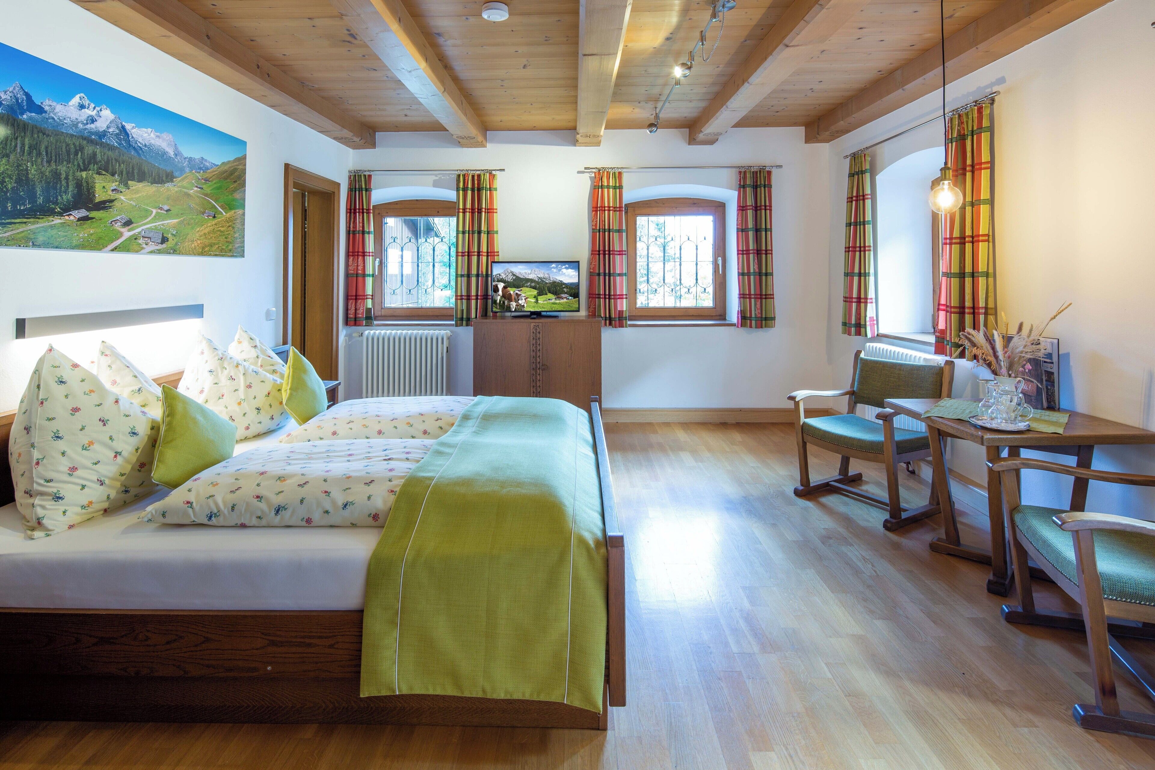 A bedroom with a bed, a desk, and a chair. There is a window with curtains and a painting on the wall.