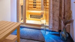 Ein Saunaraum mit Holzbänken und einer Glastür, eine Bank vor der Tür und einer Zierpflanze.