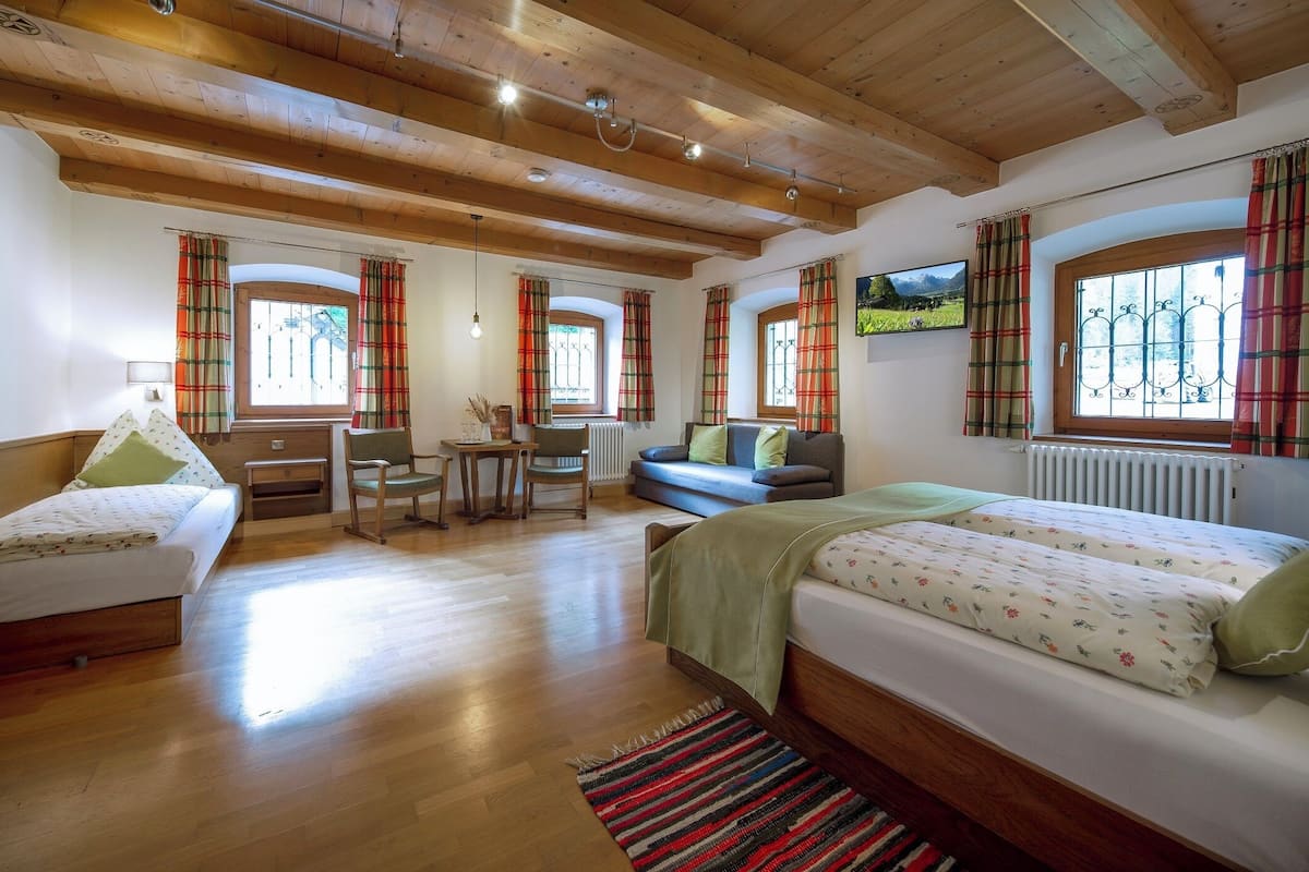 Una habitación con vigas de madera, una cama, un sofá, un escritorio y un televisor en la pared.