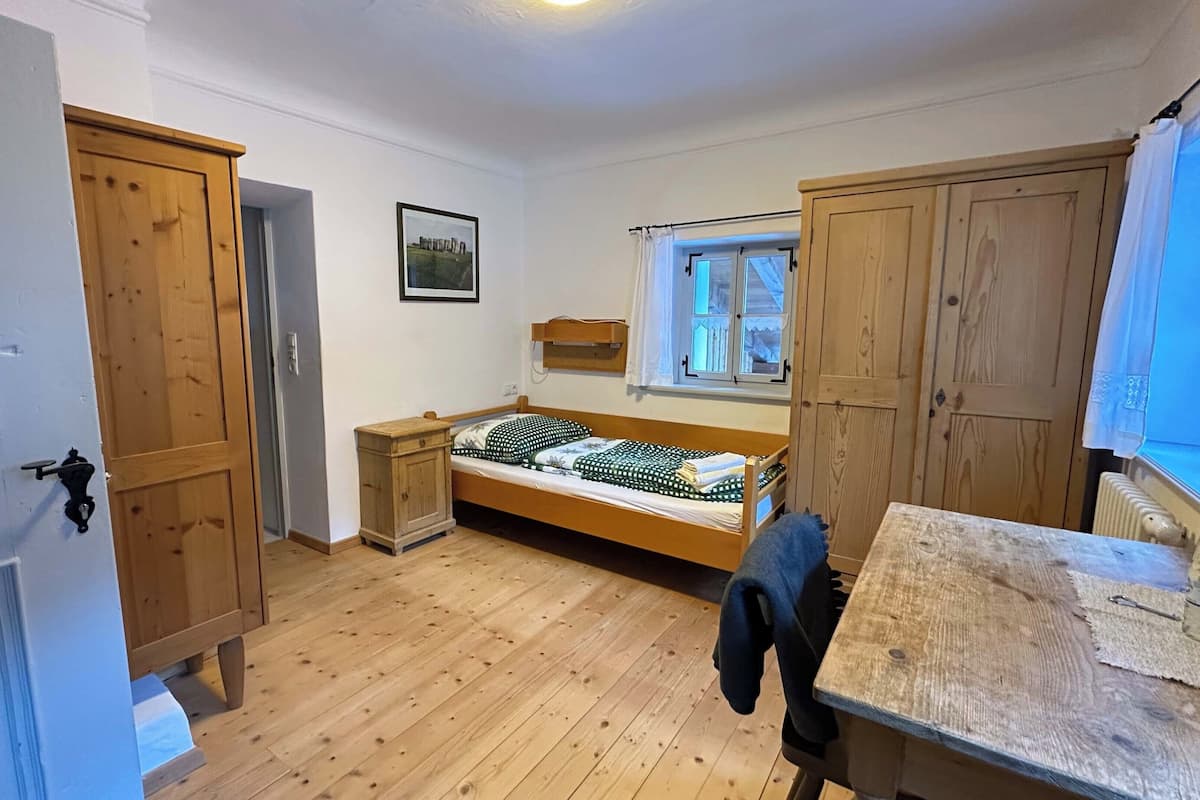 Una habitación pequeña y ordenada con una cama individual, un armario de madera y una ventana.