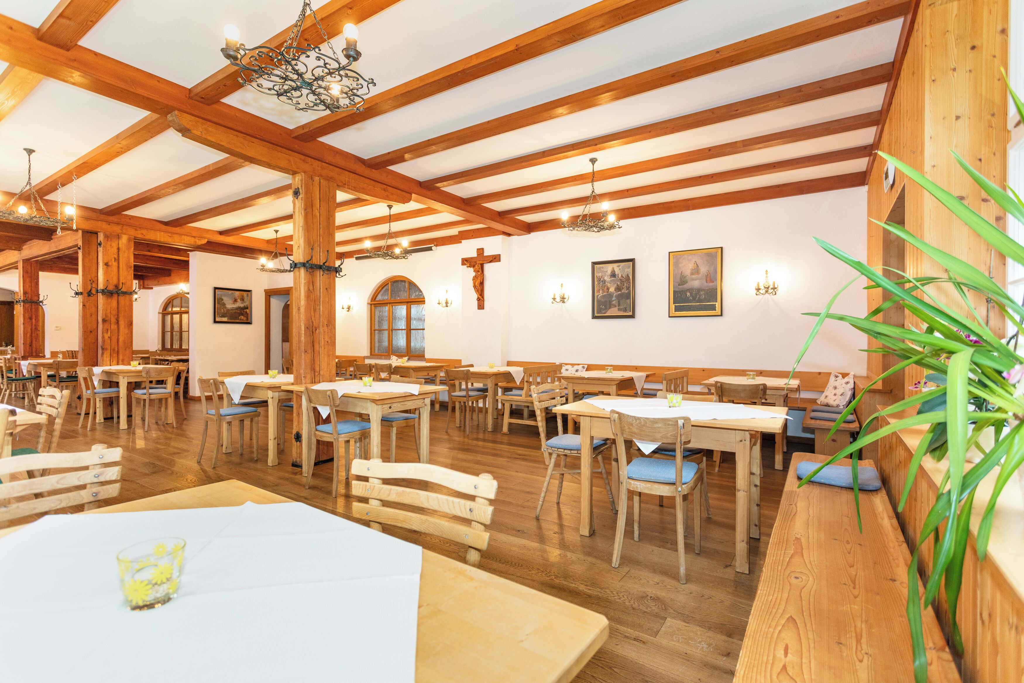 Uma sala de jantar com mesas e bancos de madeira, vigas de madeira aparentes e lustres.