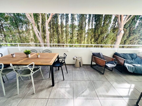 Un patio con una mesa de madera, sillas, una planta pequeña en maceta y un sofá con cojines.