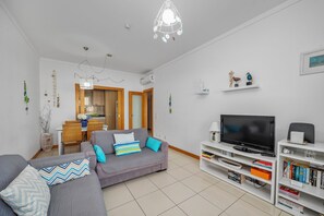 A living room with a grey sofa, a TV, and a bookshelf. - Super Cute 1-Bed Beachfront Pool View Apartment (Albufeira)
