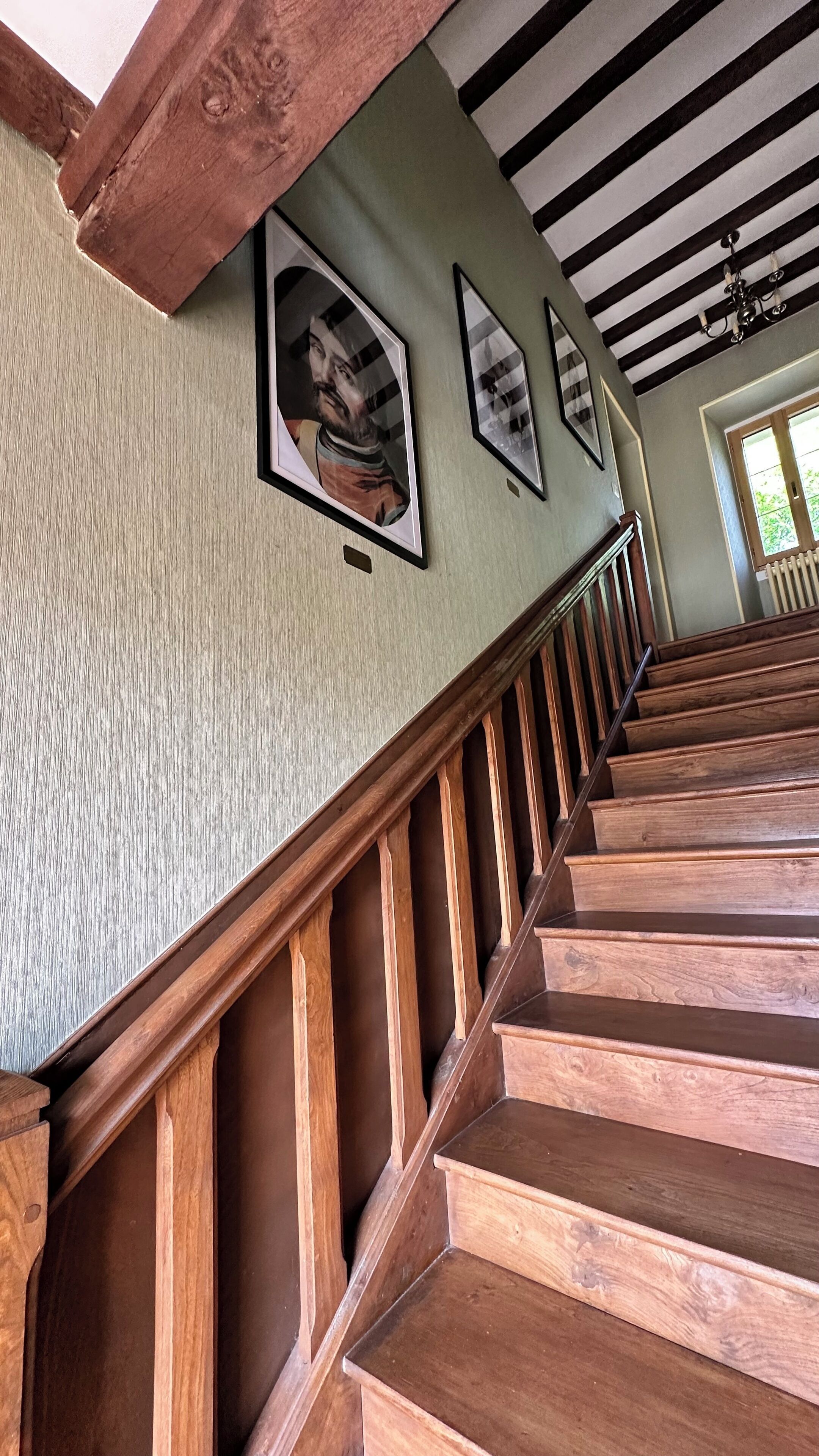 En trappa med trästeg och en vägg med en tydlig struktur, där det hänger inramade bilder.