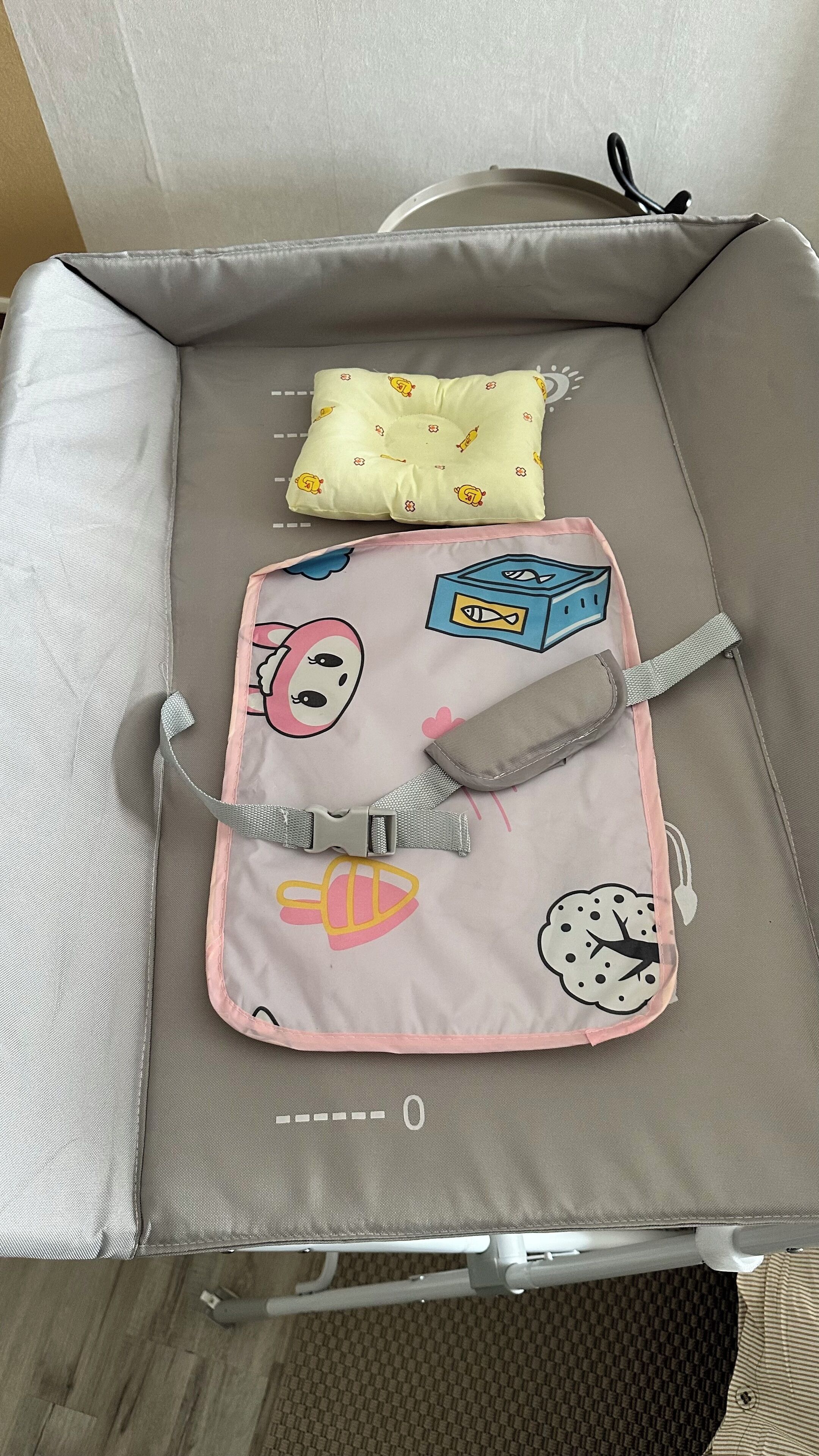 Une valise de voyage avec un intérieur gris, un sac de voyage rose et blanc orné de motifs de dessins animés, et un coussin jaune à motifs.