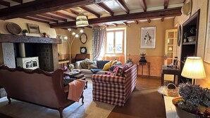 A cozy living room with a fireplace, a sofa, a checkered ottoman, and a lamp.
