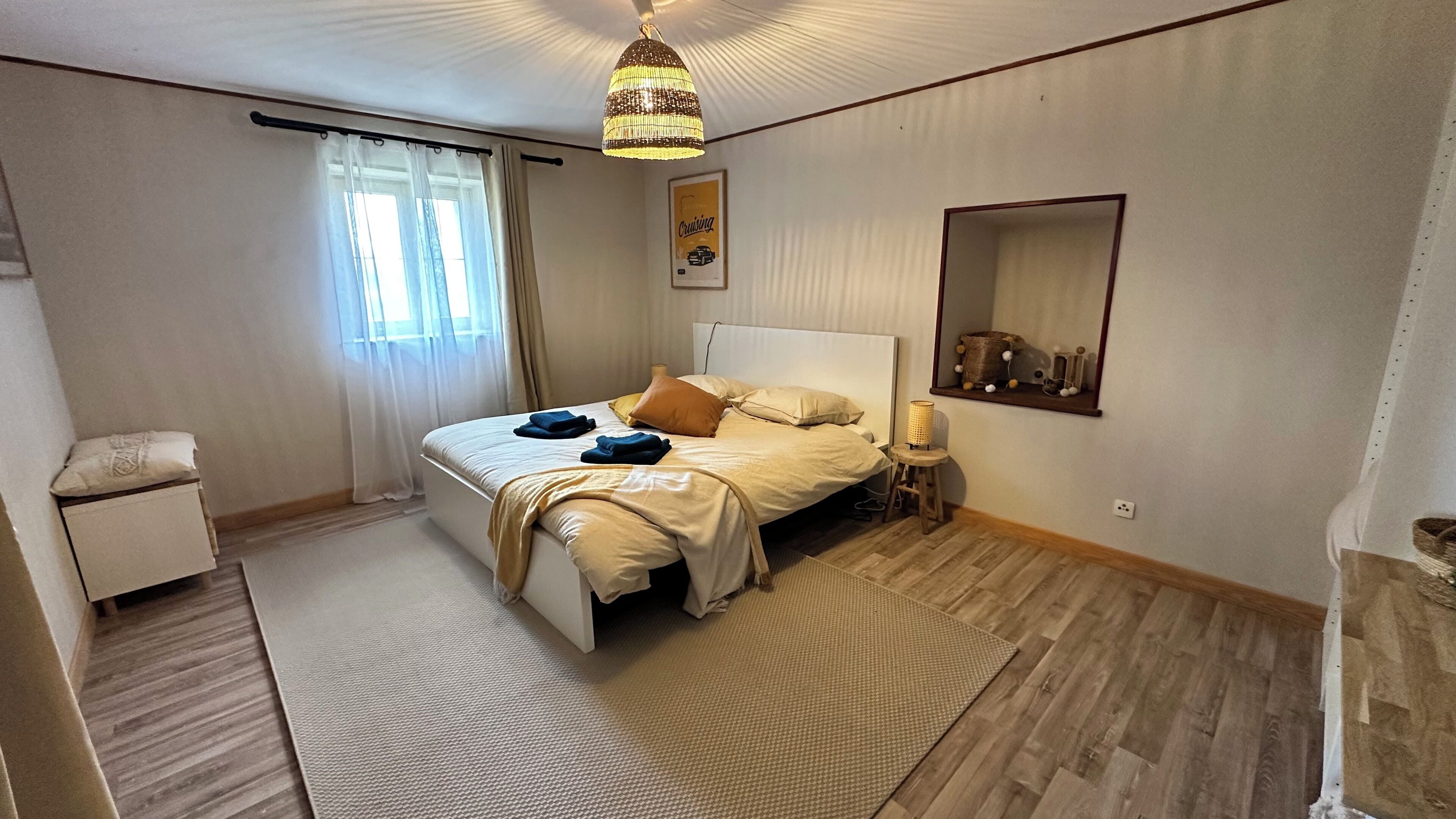 Et soveværelse med seng, sengebord, lampe og pendel.