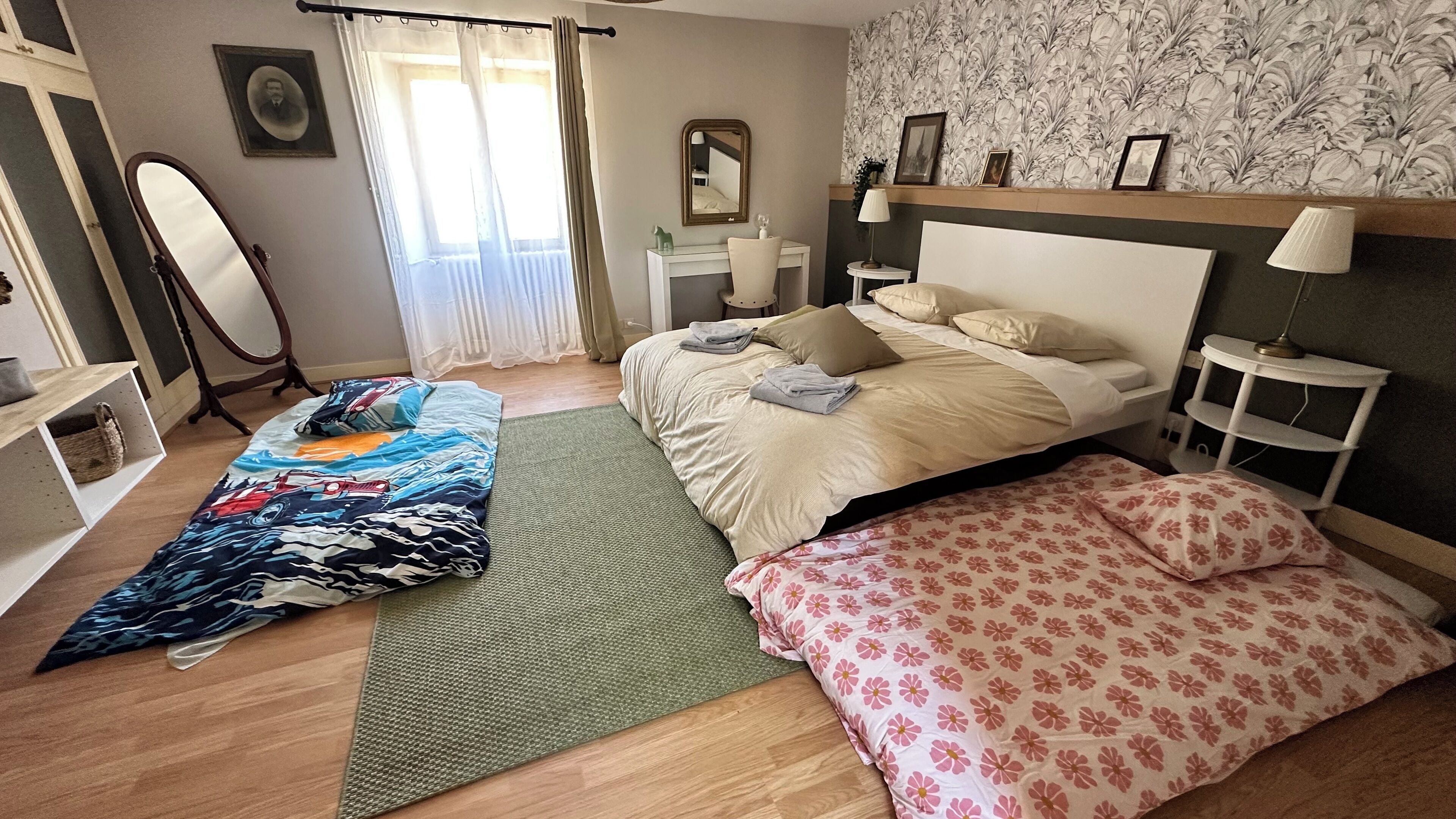 Ein Schlafzimmer mit Bett, Nachttischen, einem Spiegel und einem Fenster mit Vorhängen.
