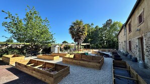 A courtyard with raised garden beds, outdoor seating, and a stone building.