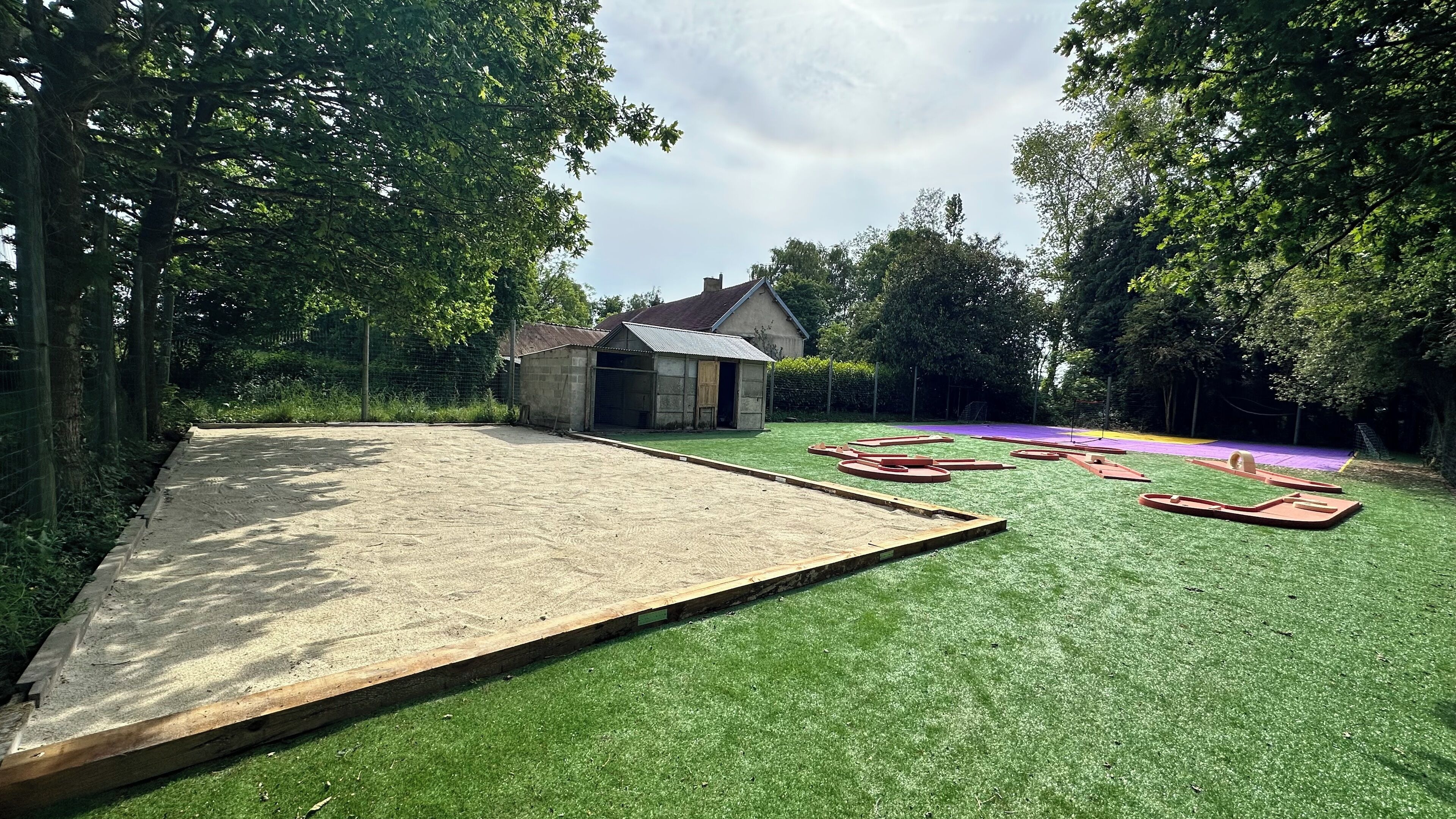 Un jardin avec une pelouse artificielle, une rampe en bois et un petit abri de jardin.