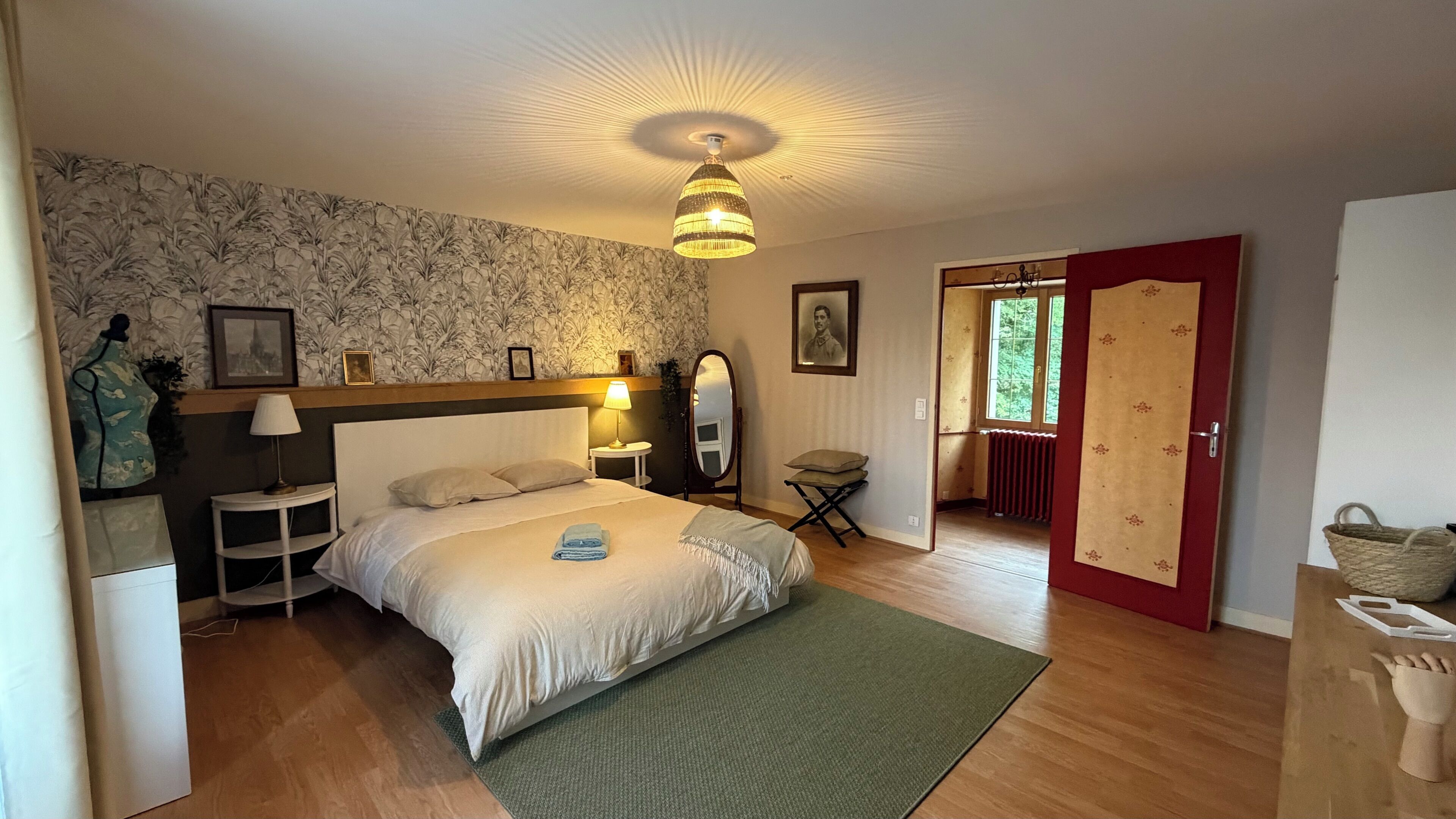 A hotel room with a bed, a bedside table with a lamp, a mirror, a window, and a door.
