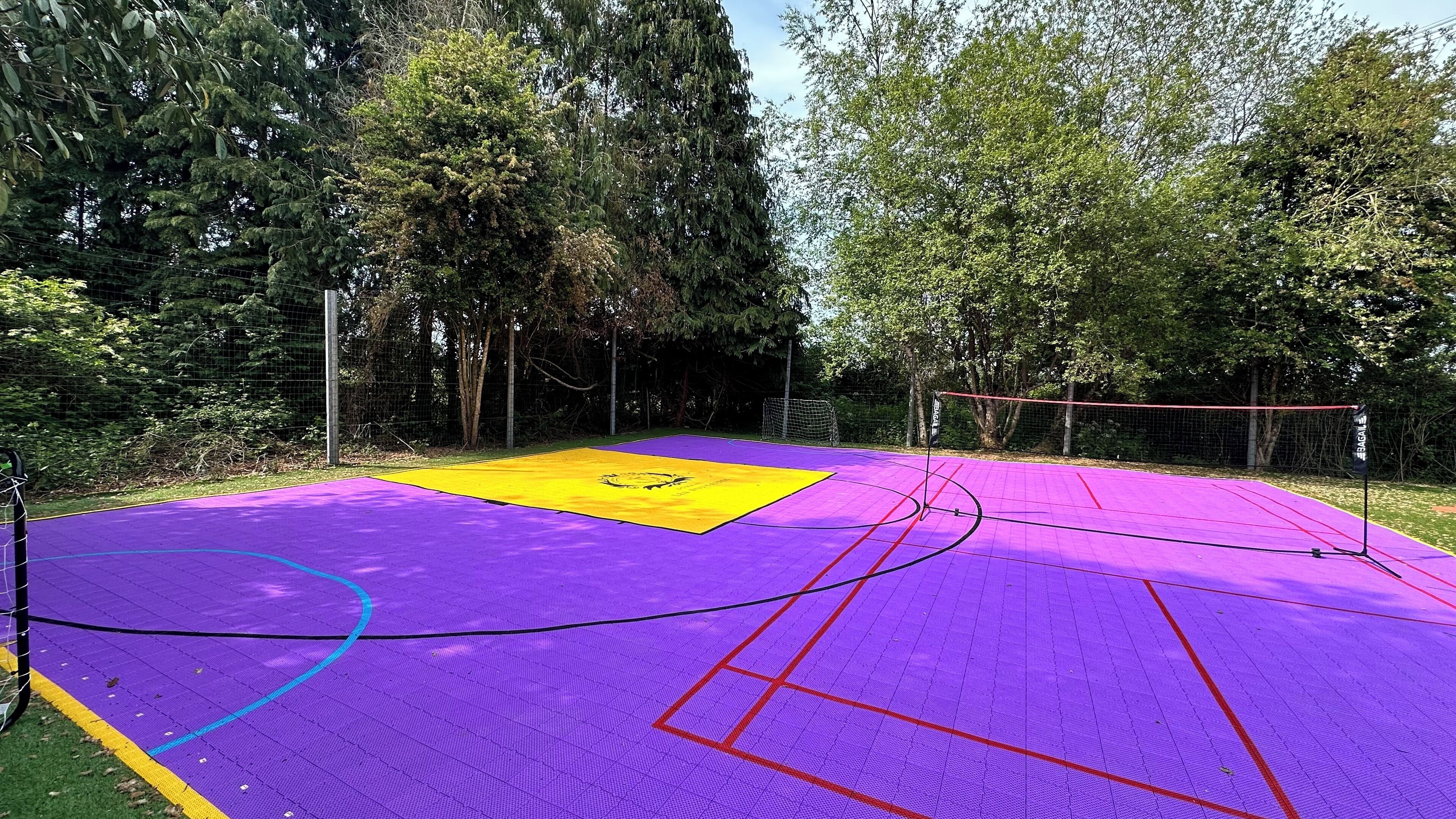 Ein Sportplatz im Freien mit einer violett-gelben Spielfläche, umgeben von Bäumen.
