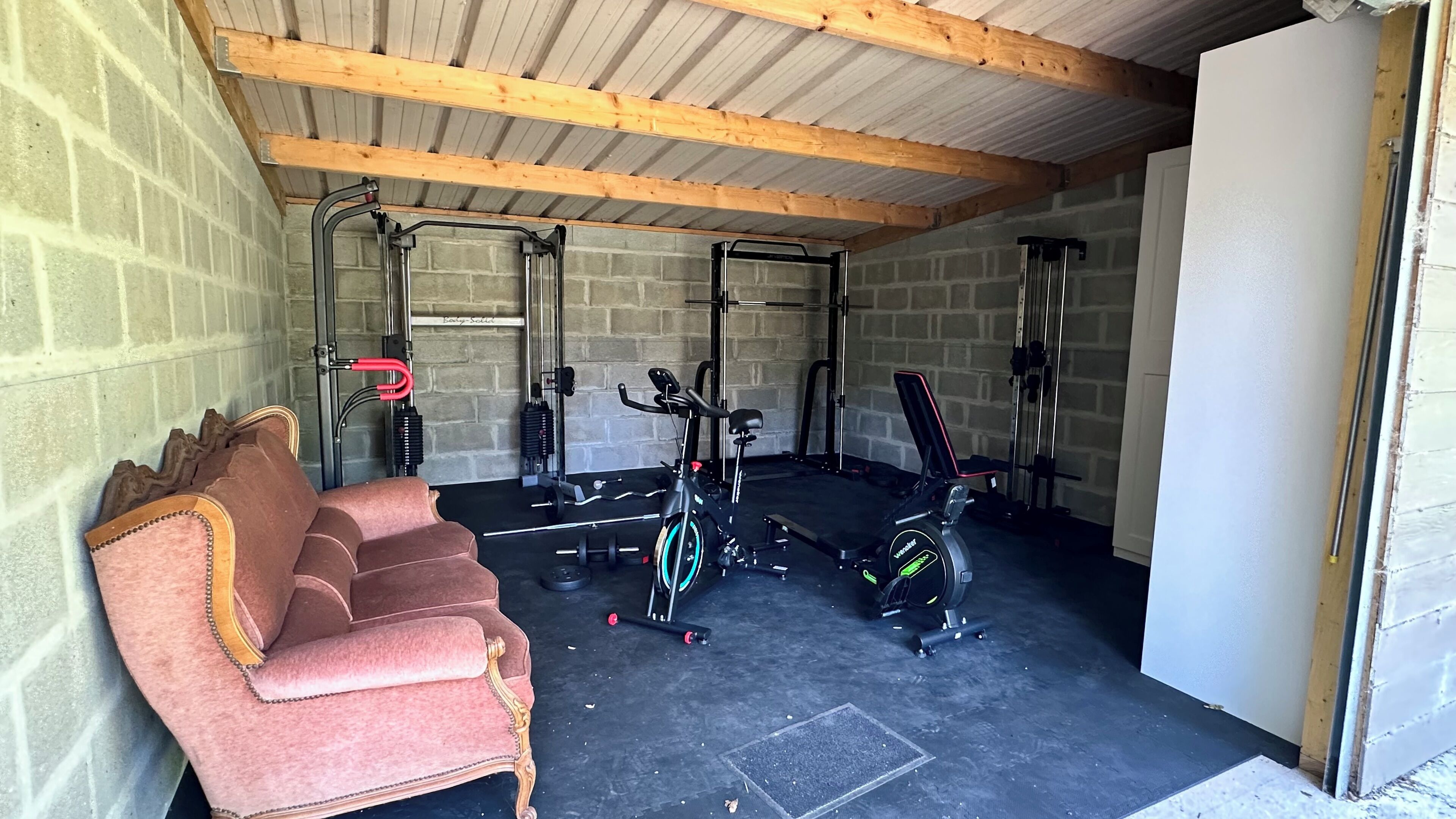 A gym with exercise equipment, a bench, and a red sofa.