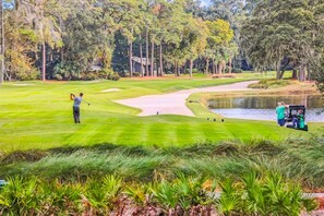 En golfbane med et vandhazard, sandbunker og en klubhus i baggrunden.