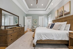 A bedroom with a large bed, wooden headboard, a dresser, and a mirror. There are doors leading to other rooms.