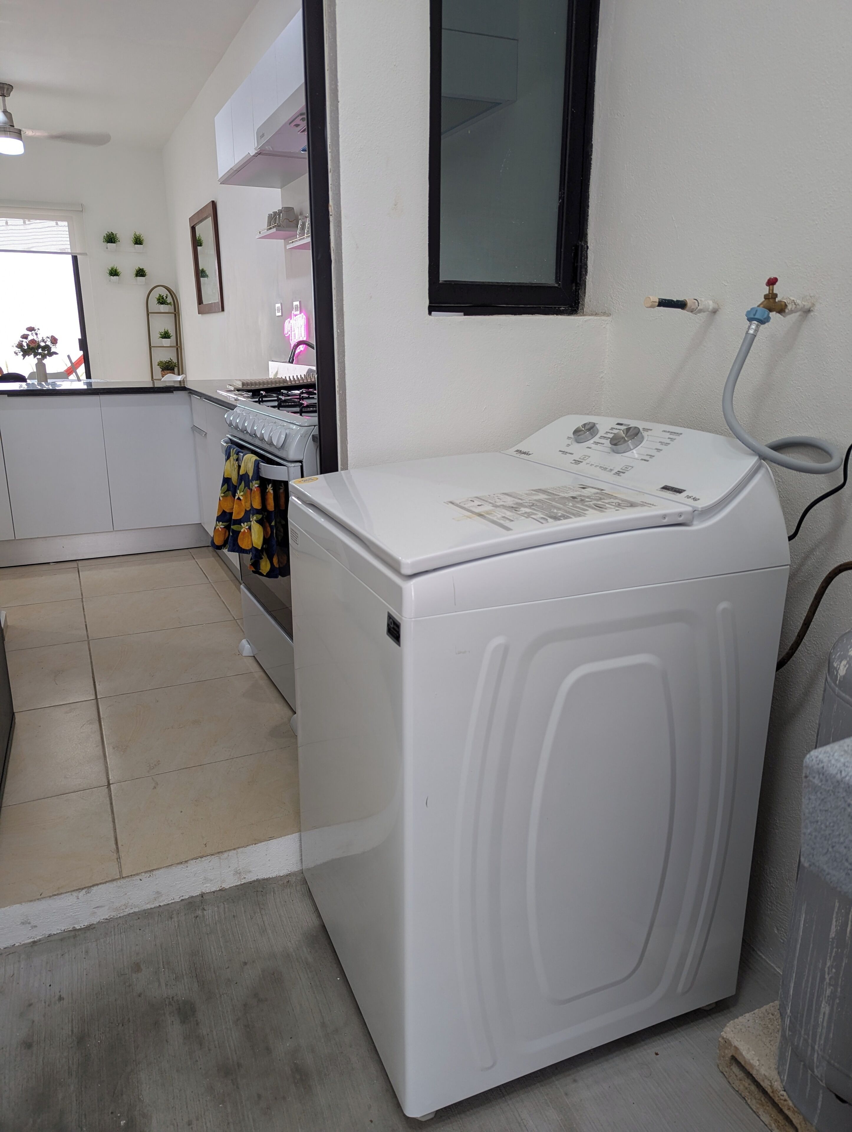 Een compacte keuken met een ingebouwde wasmachine en droger, een klein aanrecht en een raam met zonwering.