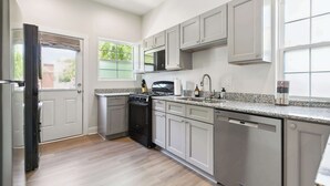 A modern kitchen with grey cabinets, a stainless steel dishwasher, and a black stove. - Funky & Fun! 1BR Apartment, Ground Floor (Baton Rouge)