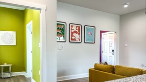 En modern inredning med en grön accentvägg, en gul soffa och ett köksområde med bänkskivor i granit.