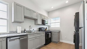 A modern kitchen with grey cabinets, a dishwasher, a stove, and a refrigerator. - Red Stick Proud - 1BR Apartment, 2nd Floor (Baton Rouge)
