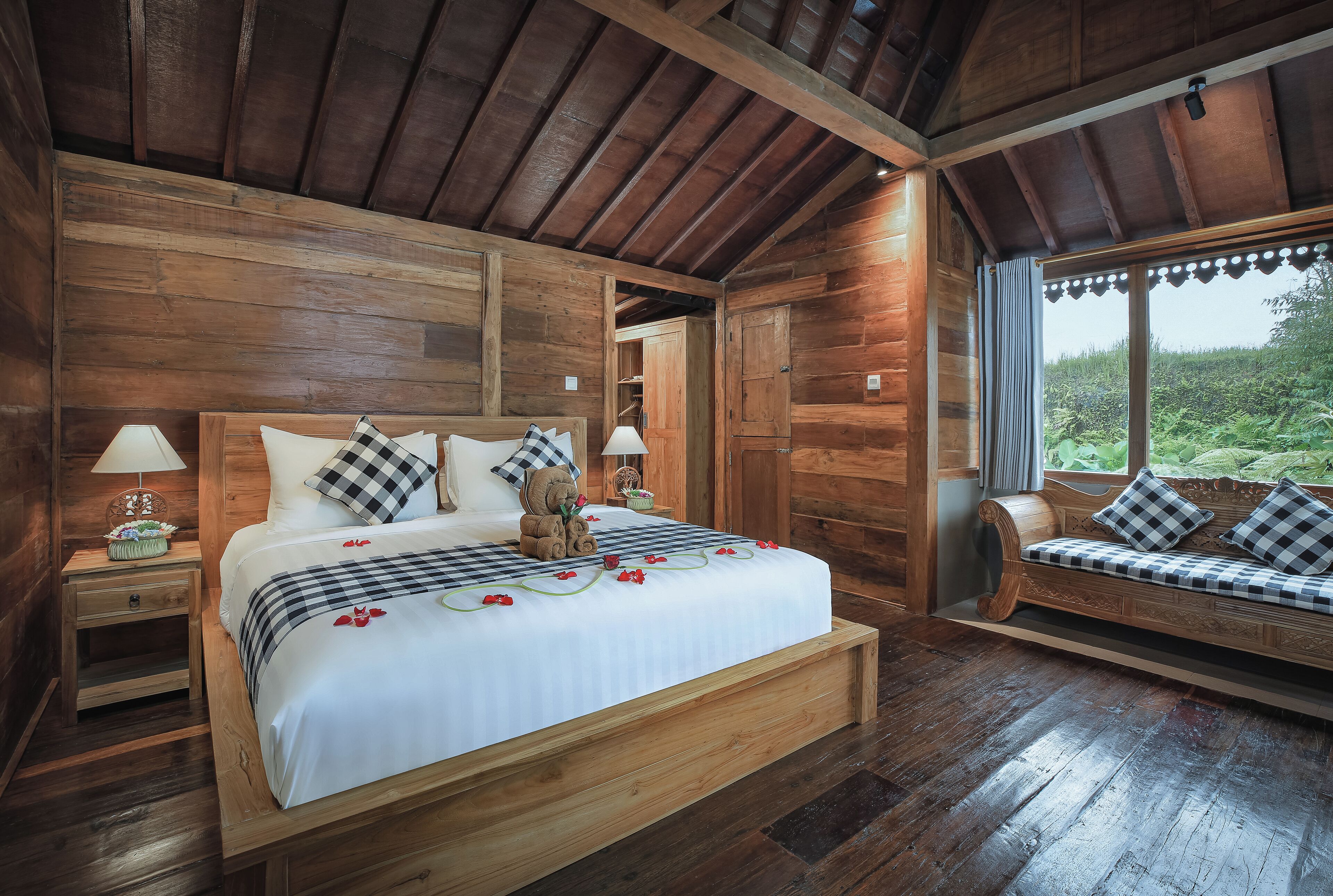 A wooden cabin-style bedroom with a large bed, a bench, and a window with curtains.