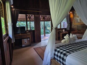 A bedroom with a bed, a desk, a TV, and a view of the outdoors.