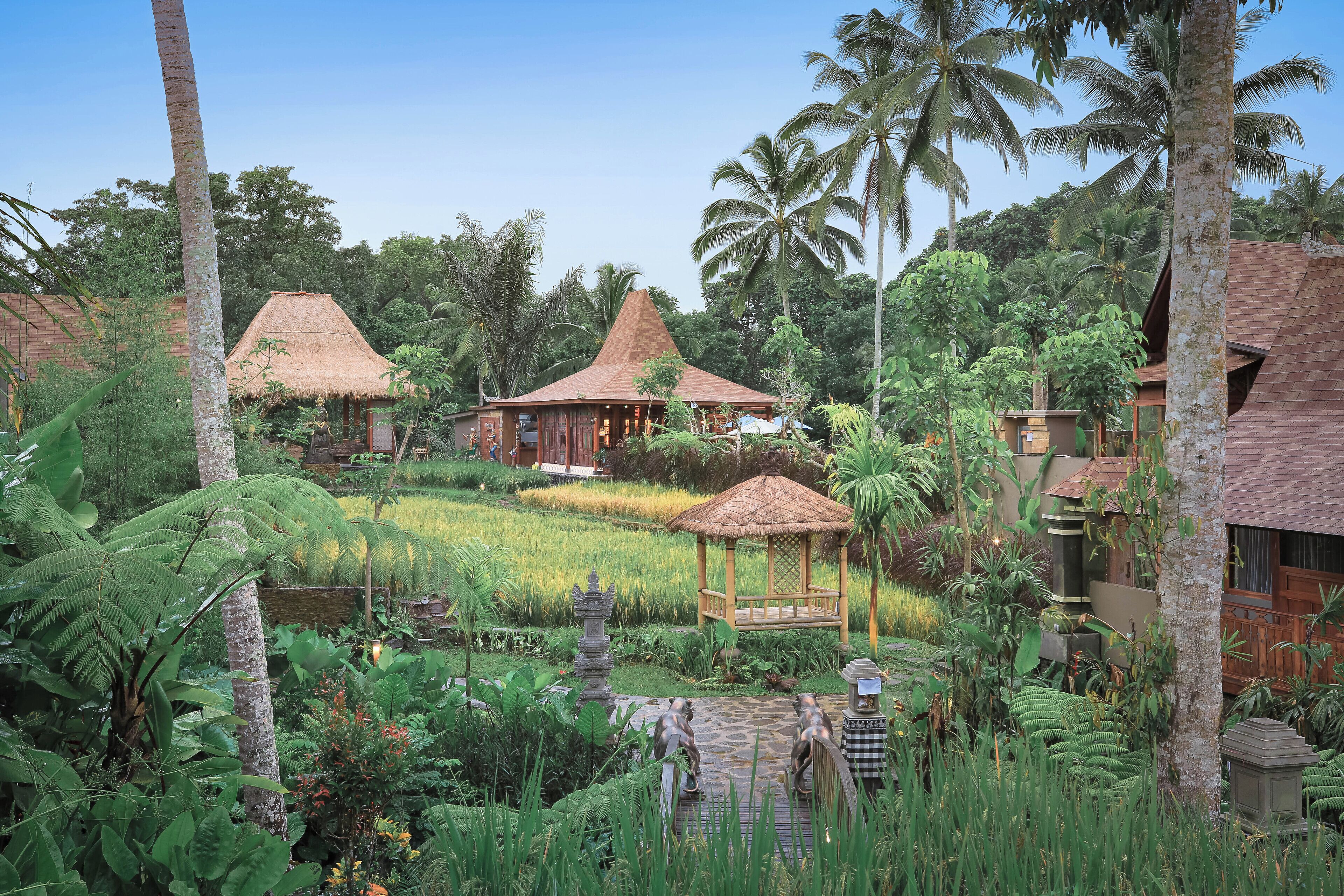 A tropical resort with thatched-roof huts, lush greenery, and a serene garden setting.