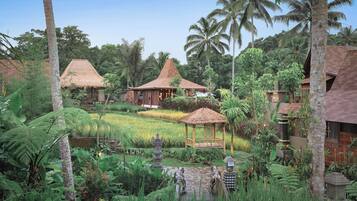 A tropical resort with thatched-roof huts, lush greenery, and a serene garden setting.