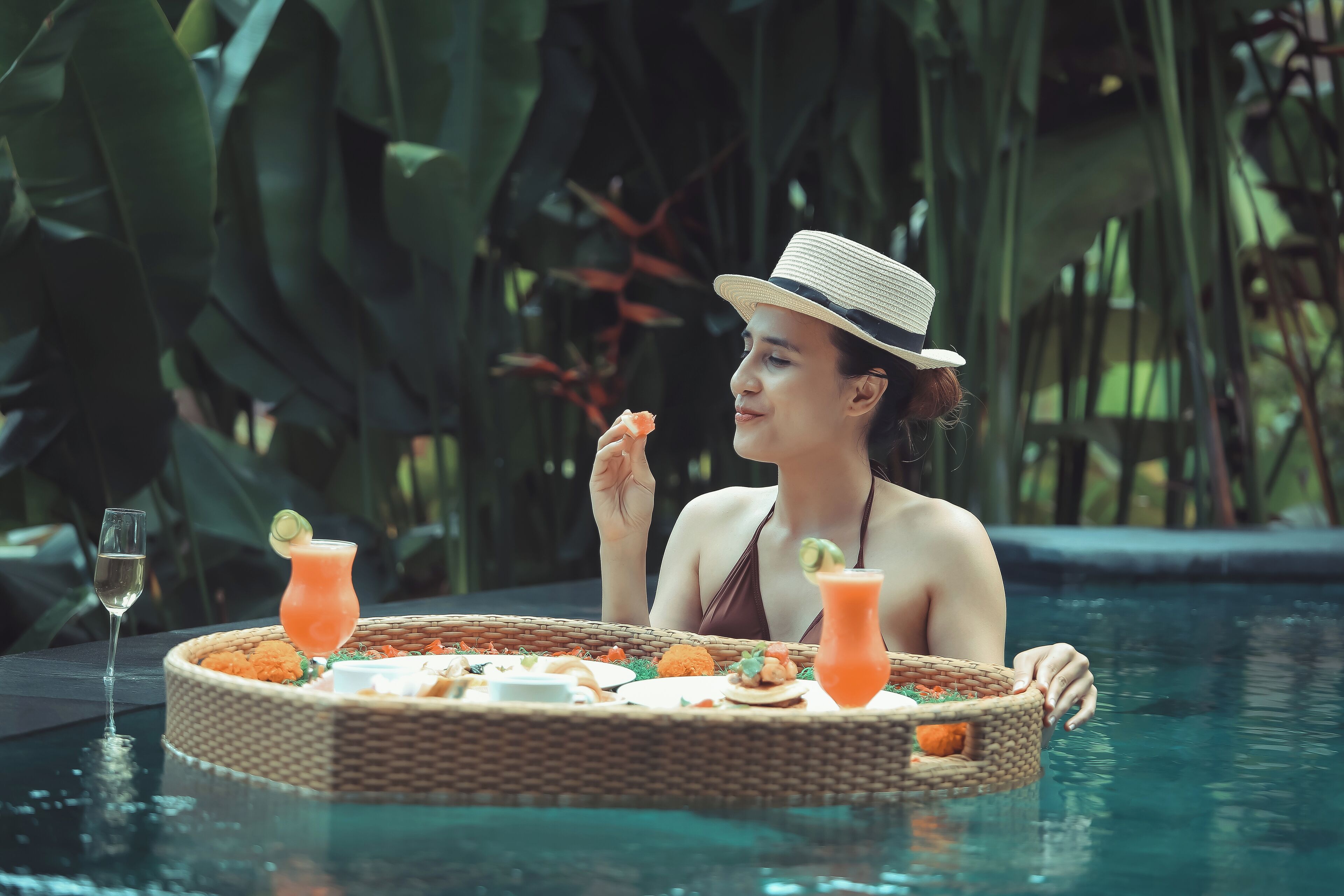 A person relaxing in a pool with a floating tray of food and drinks.
