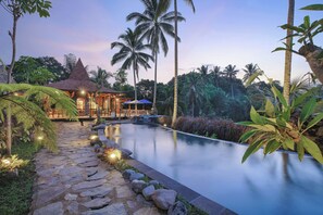 A serene pool area with a stone pathway, palm trees, and a thatched-roof structure. - Lawani Resort (Sebatu)