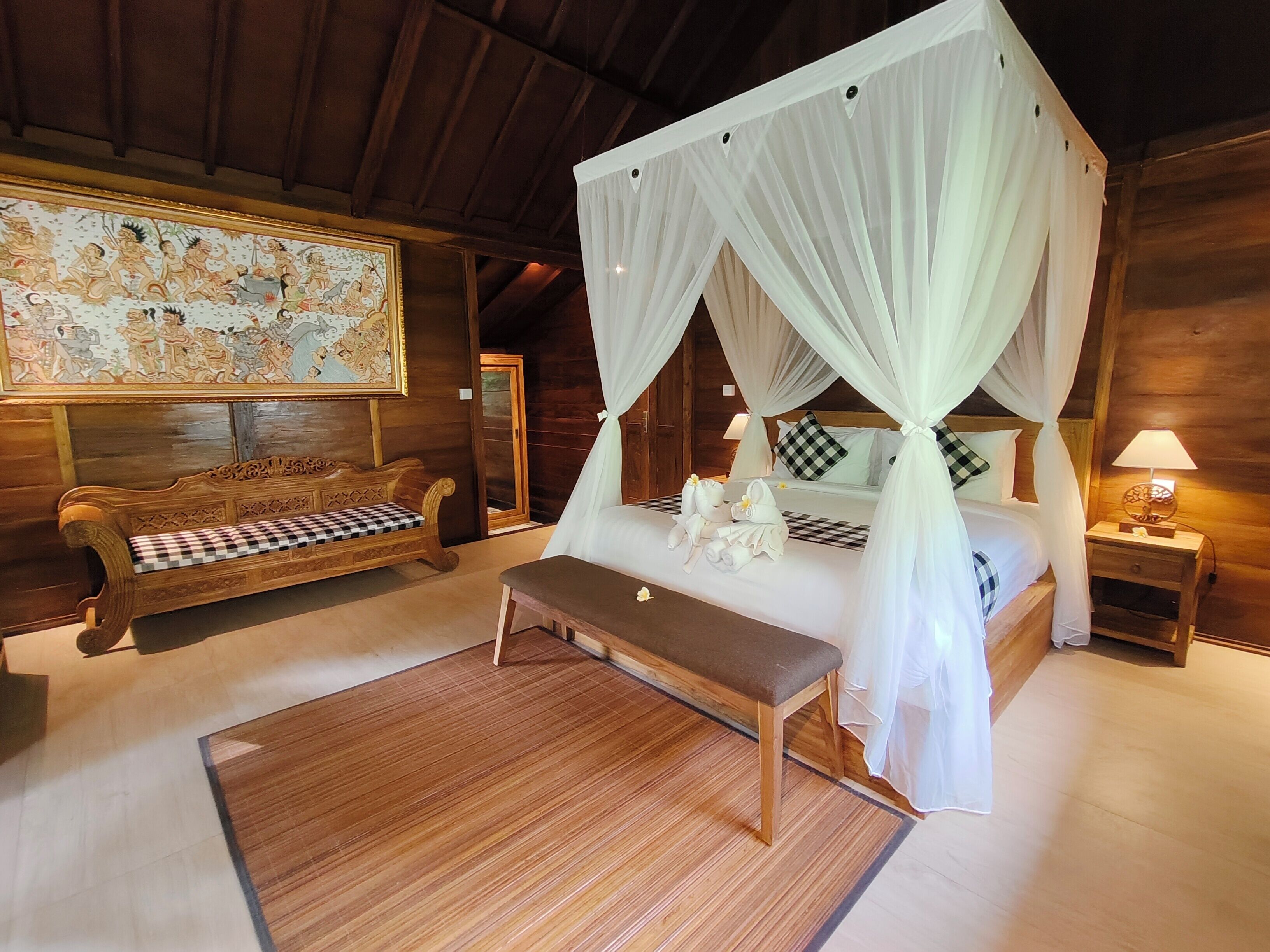 A bedroom with a four-poster canopy bed, a wooden bench, a checkered sofa, and a large mural on the wall.
